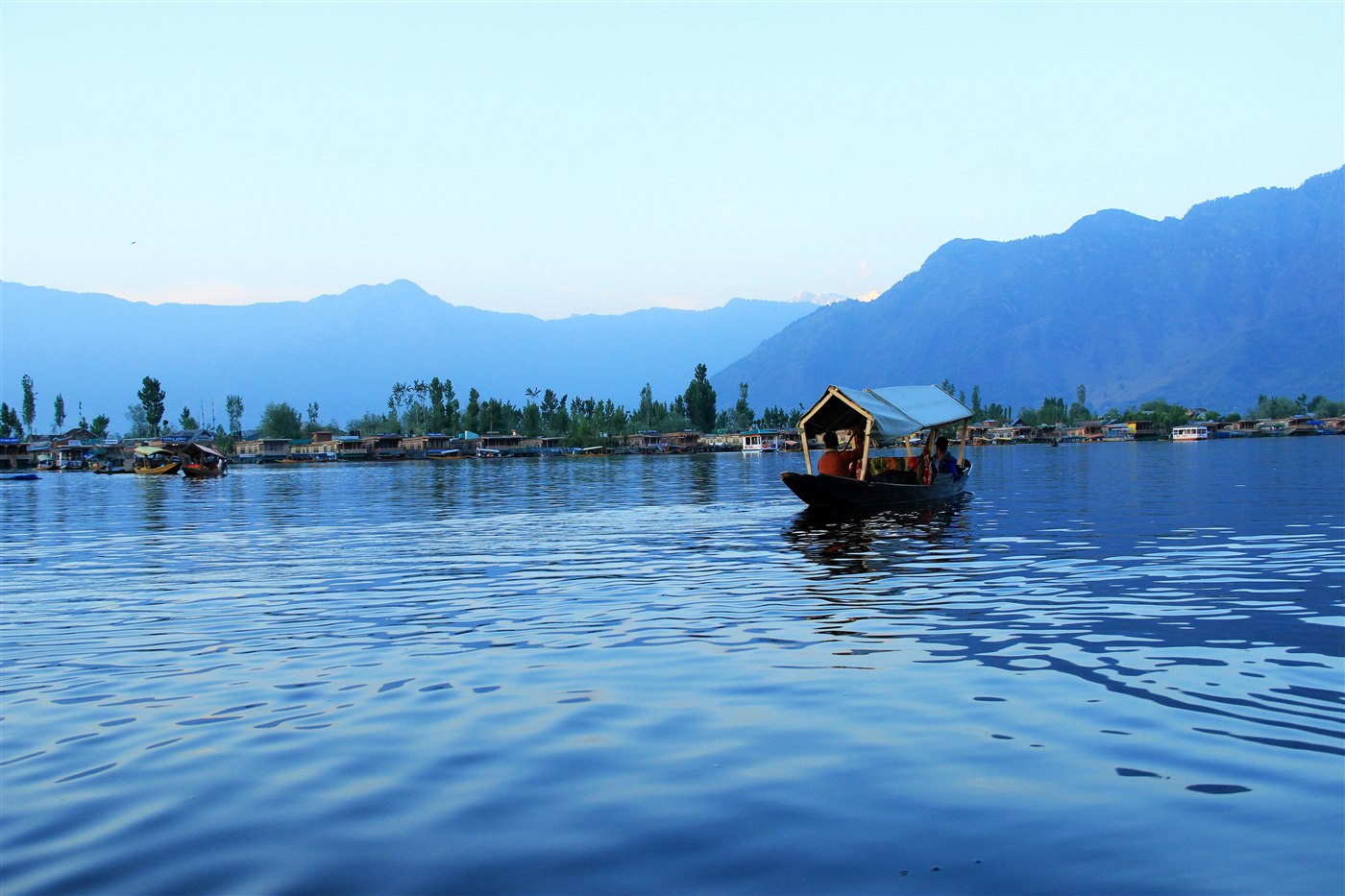 A shikara boat crossing Dal Lake at dusk with houseboats and mountains behind, Srinagar, Kashmir