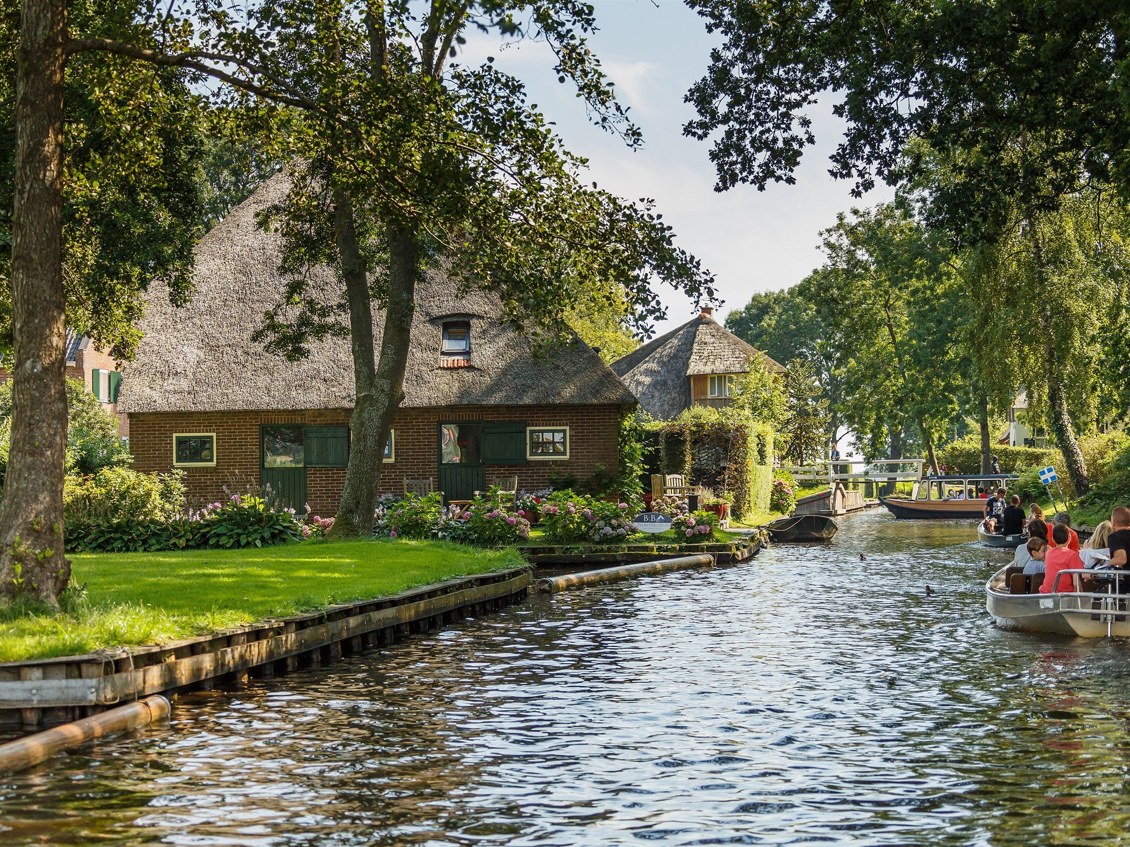 Thatched-roof farmhouse beside a canal with a tour boat passing, Giethoorn