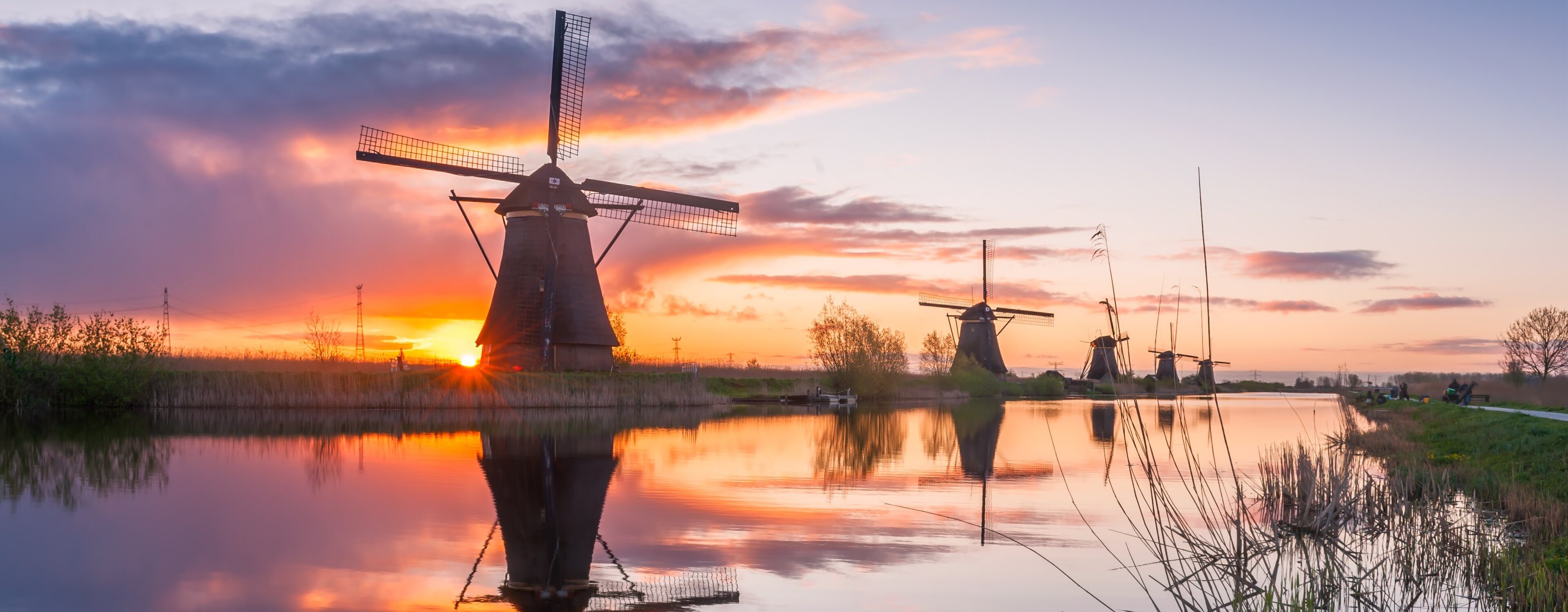 Traditional windmill reflected in a still canal at sunrise, with more windmills in a row behind it, Kinderdijk, Netherlands