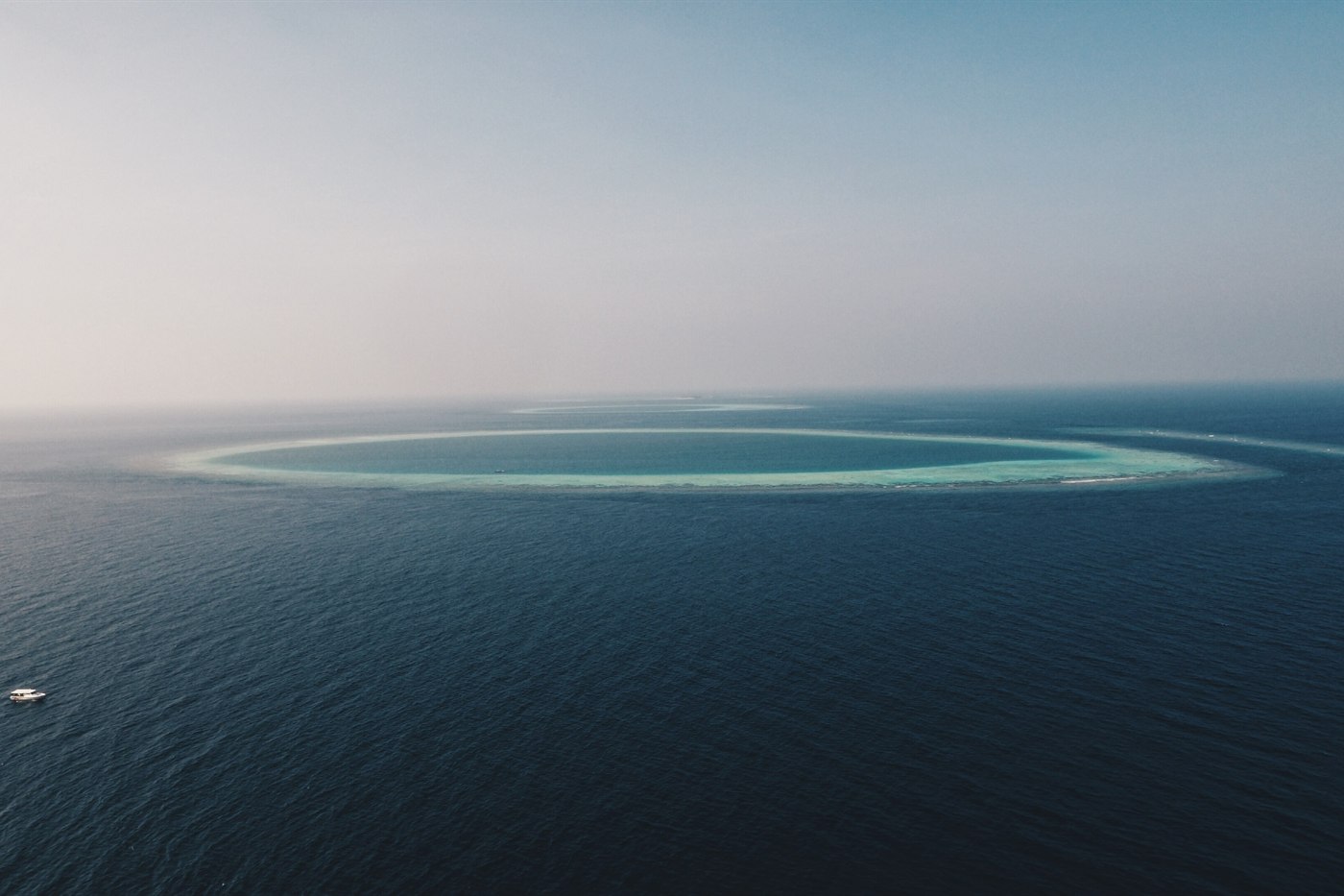 Aerial view of a ring-shaped atoll reef in the Maldives, turquoise lagoon inside a pale sandbar
