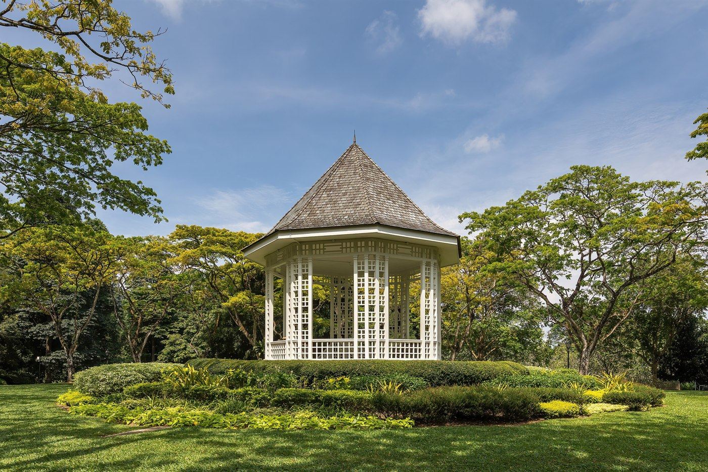 The white Bandstand among tall trees on the lawns of the Singapore Botanic Gardens