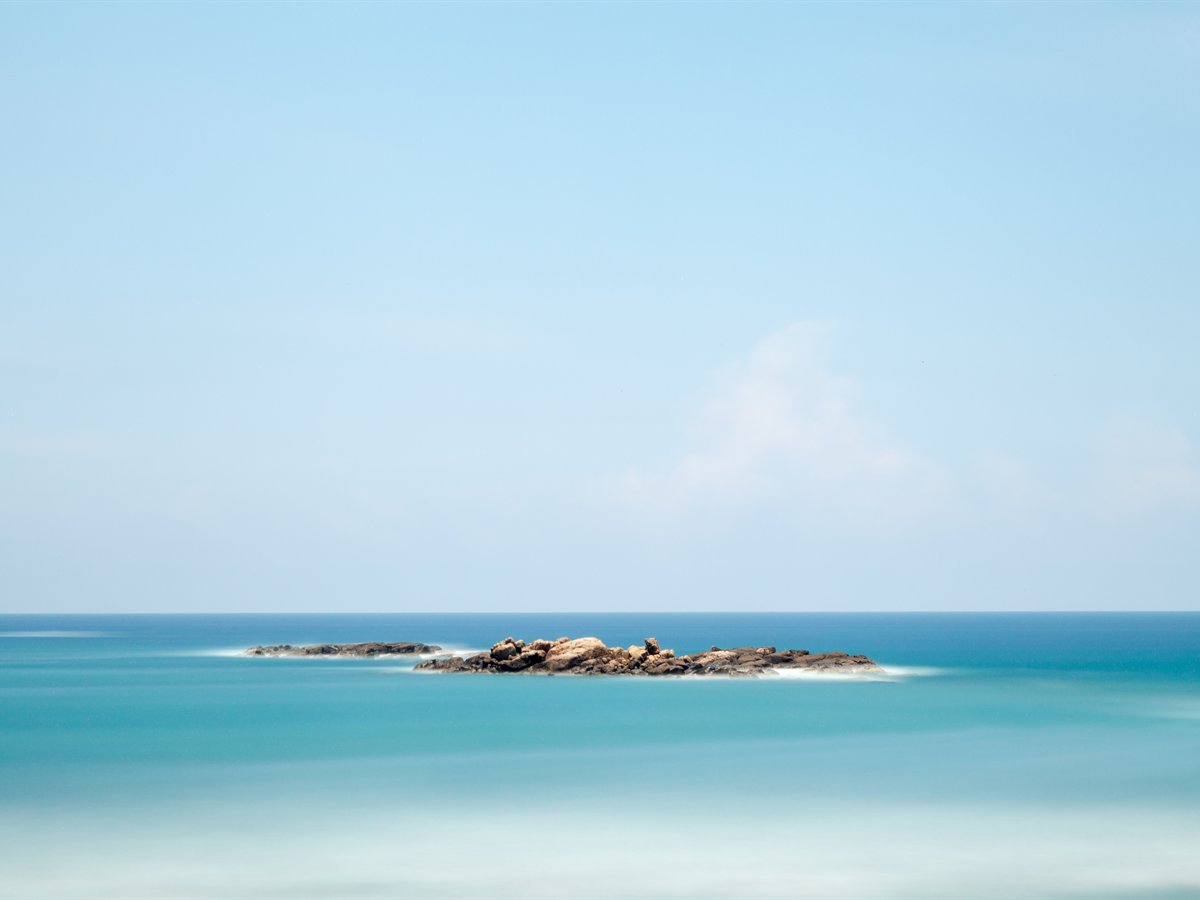 Calm turquoise sea and a low rocky islet off Unawatuna, near Galle, Sri Lanka