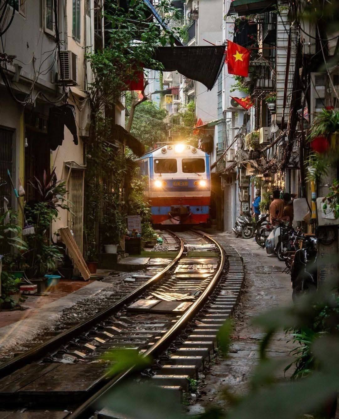 A train passing through the narrow lanes of Hanoi's Train Street at dusk