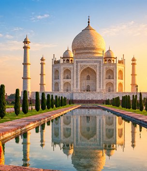 Woman in a saffron sari looking at the Taj Mahal reflected in the pool at sunrise, Agra, India